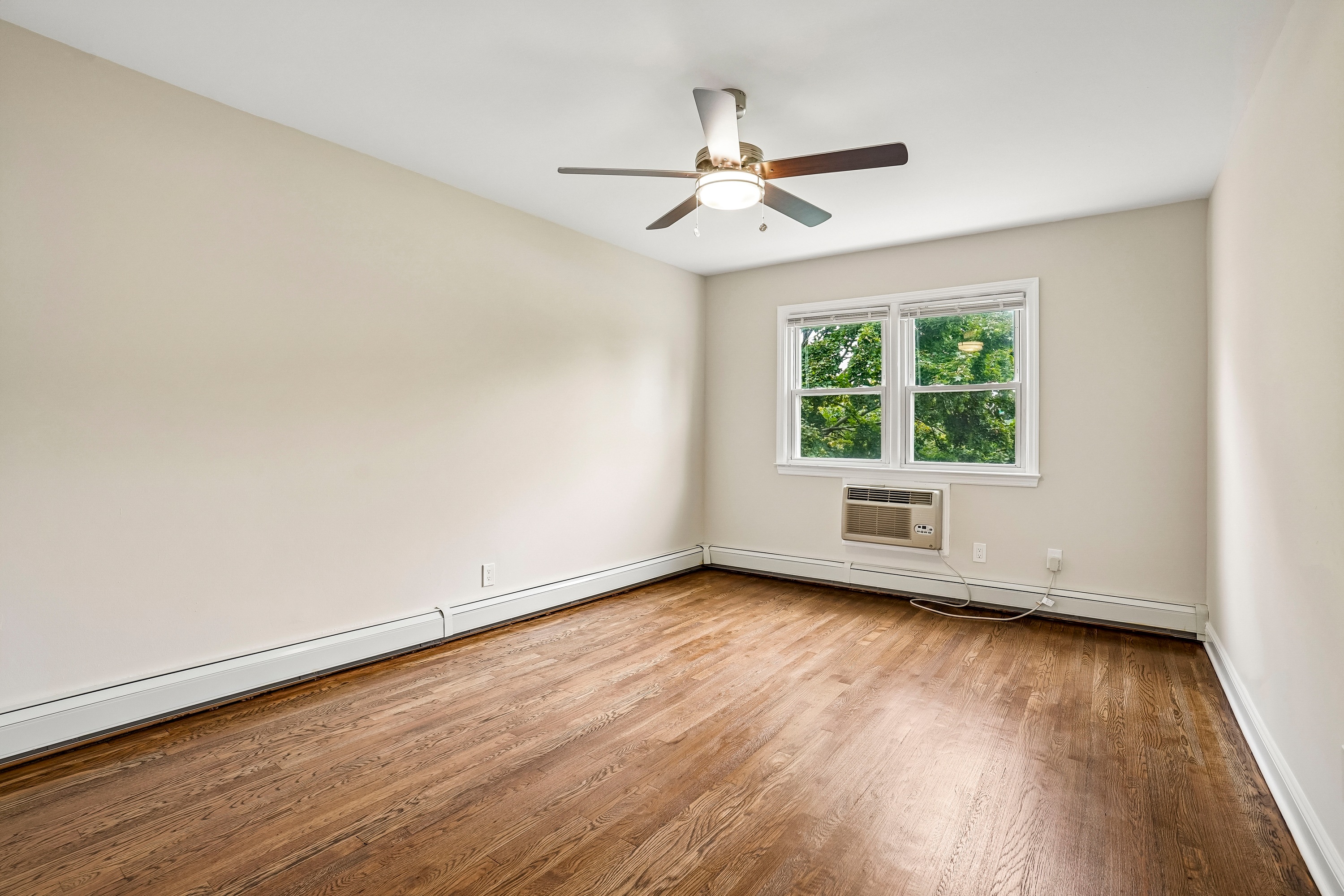 A room with a ceiling fan and a window showing greenery outside.